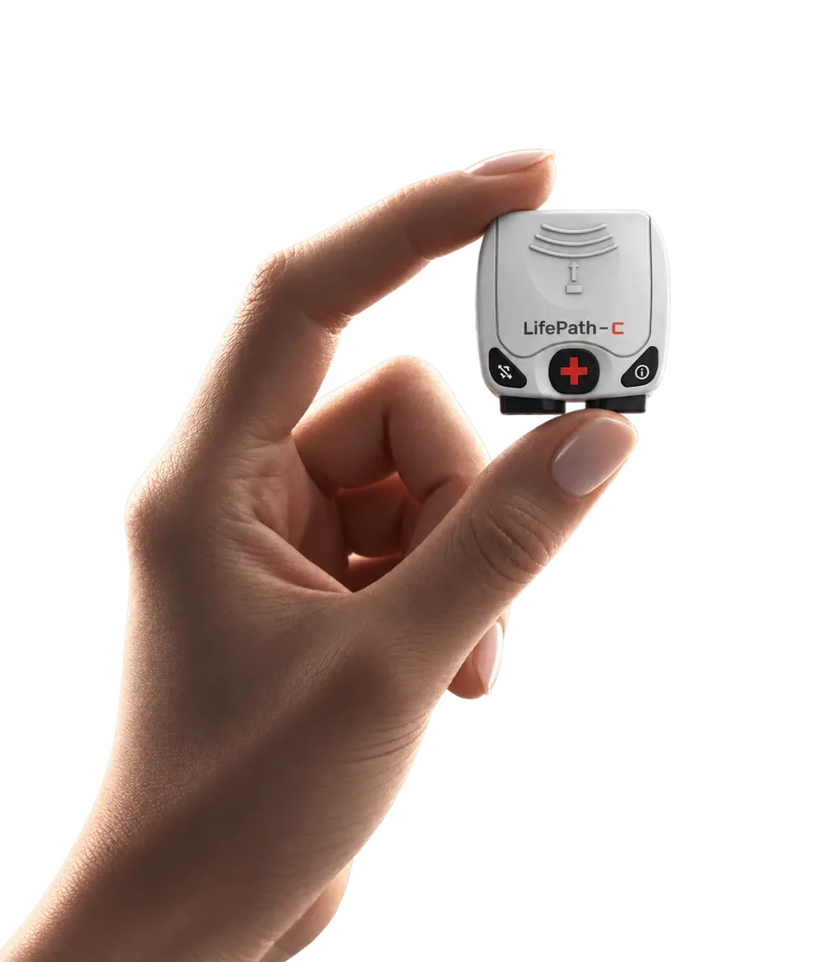 The LifePath-C monitor held between two fingers, showing its size